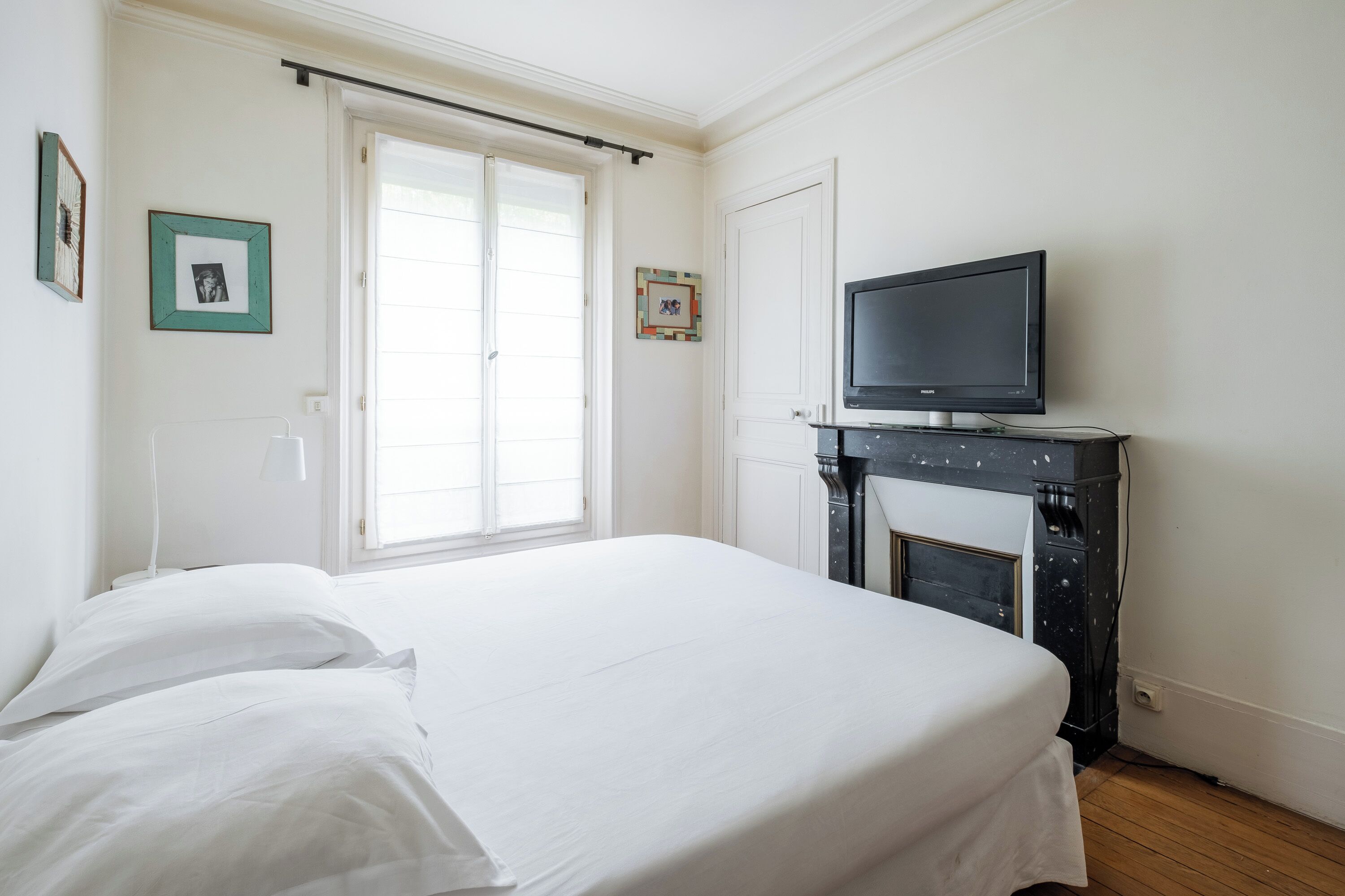 Quarto com cama, televisão sobre suporte, lareira e janela com persianas.