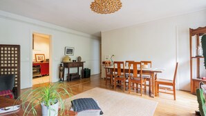 A spacious living room with a wooden dining table and chairs, a potted plant, and a patterned rug. - Boho on the Boulevard, by Veeve (Paris)