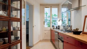 A compact kitchen with a wooden cabinet, a window with a view of greenery, and a modern stove. - Boho on the Boulevard, by Veeve (Paris)