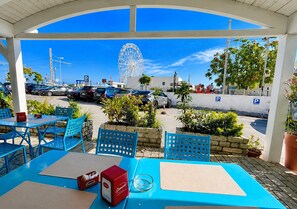 An outdoor seating area with blue chairs and tables, a Ferris wheel in the background, and a parking area with cars and people. - B&B MARINA SLEEP AND SHIP (Rodi Garganico)