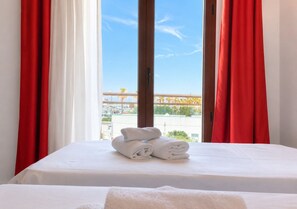 A hotel room with a bed, white linens, and a view of a marina through a large window with red curtains. - B&B MARINA SLEEP AND SHIP (Rodi Garganico)
