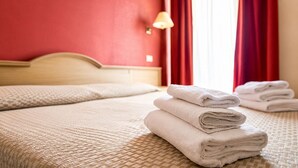 Habitación de hotel con cama, lámpara y ventana con cortinas rojas.