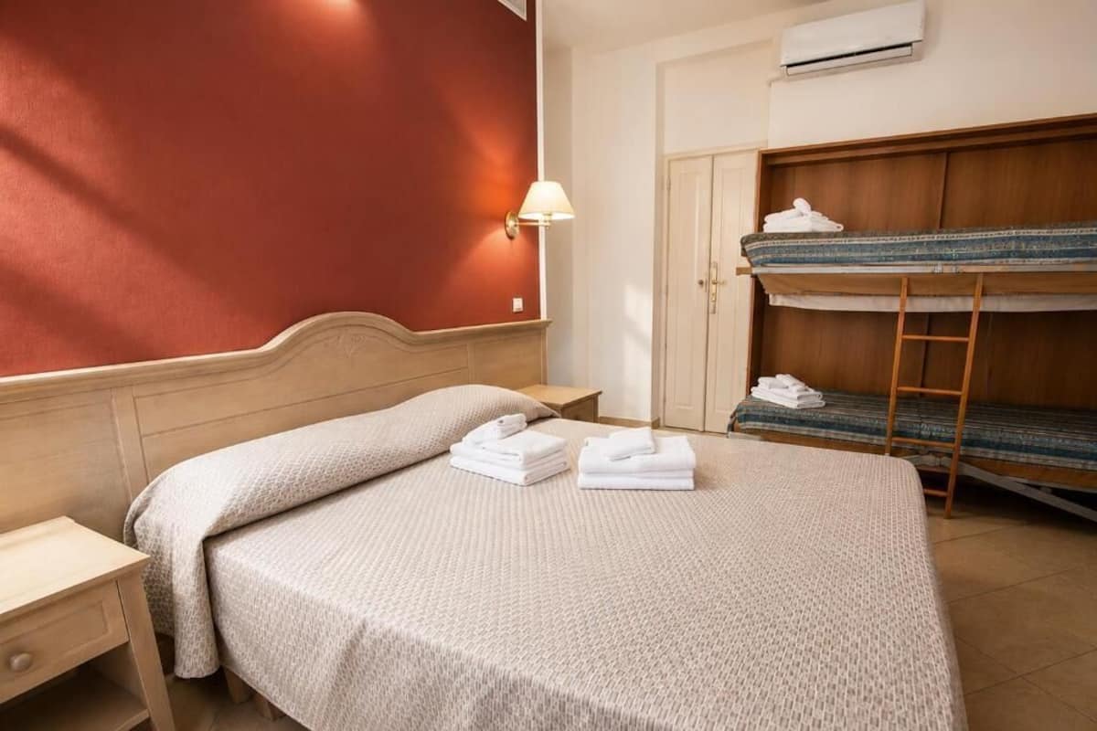 Une chambre d’hôtel avec un lit, un bureau, une armoire et un lit superposé.
