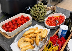 A kitchen counter with a slow cooker, a bowl of cherry tomatoes, a bowl of diced tomatoes, baguettes, and condiments. - B&B MARINA SLEEP AND SHIP (Rodi Garganico)