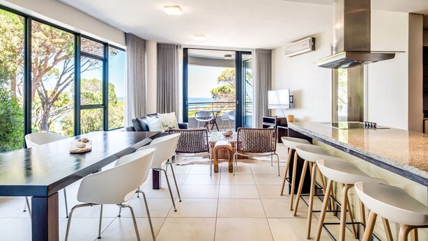 A modern kitchen with a large island, bar stools, and a view of the ocean. - Delightful Rental w Sea Views Vadi Apartment (Cape Town)