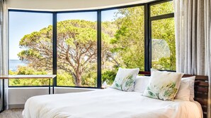 A bedroom with a large window offering a view of trees and the sea. - Delightful Rental w Sea Views Vadi Apartment (Cape Town)