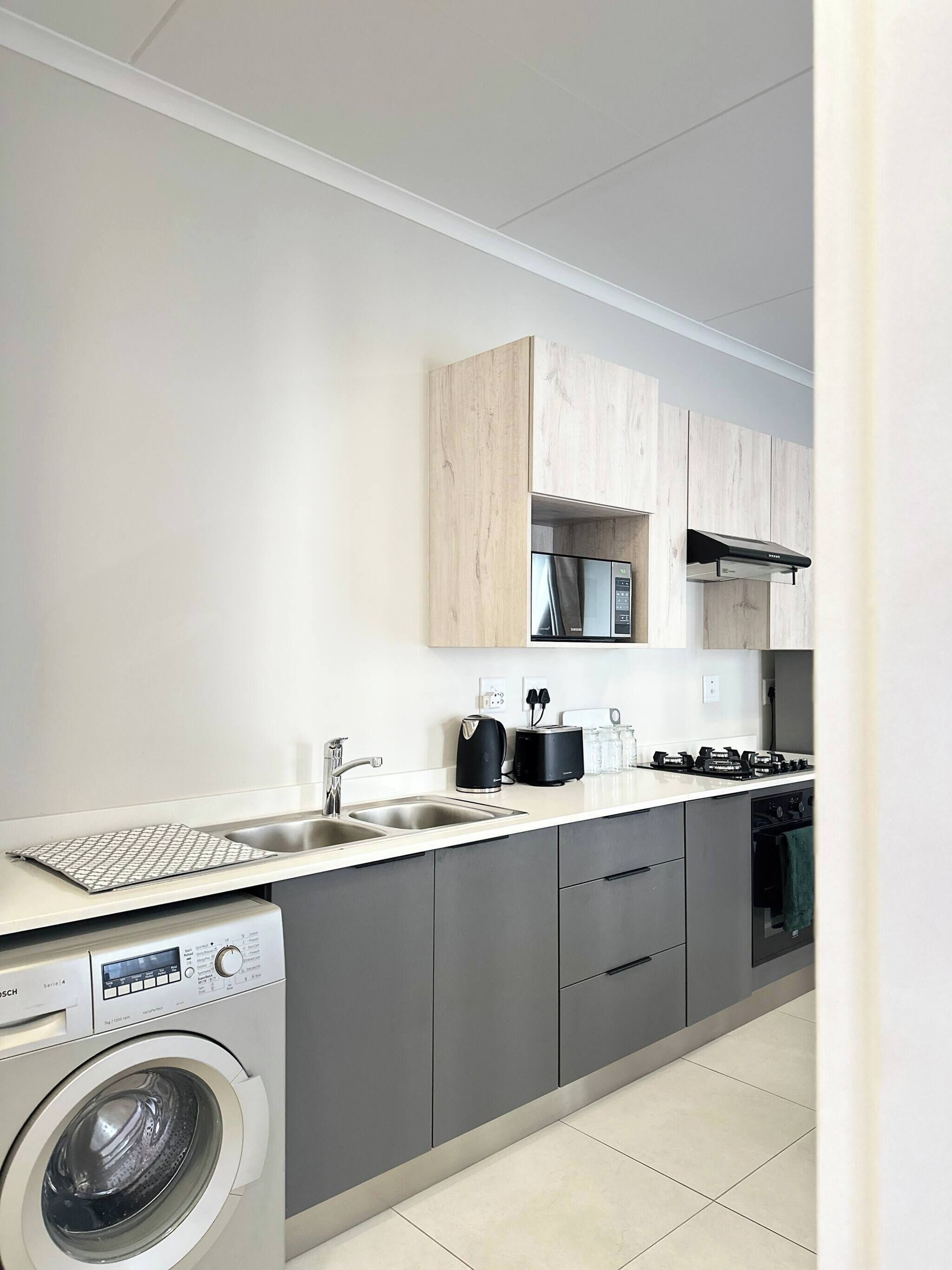 A modern kitchen with grey cabinets, a built-in washing machine, a sink, and a stove.