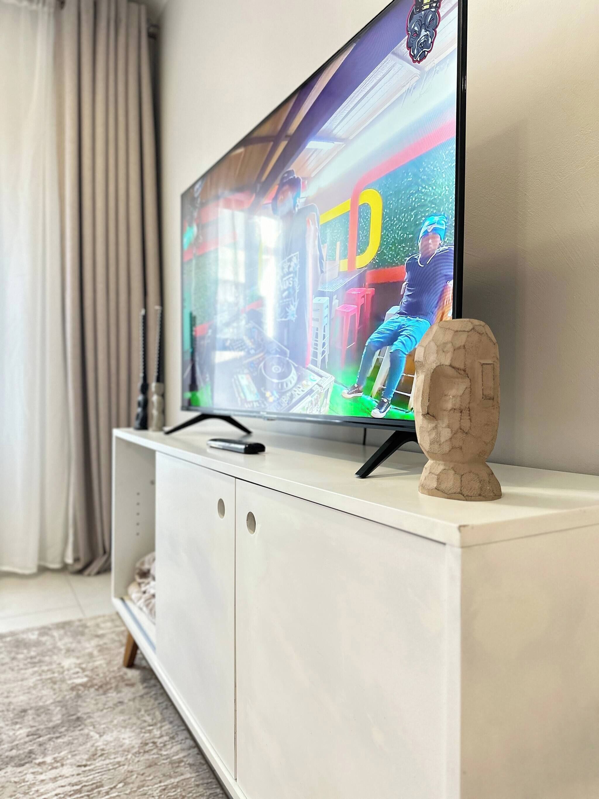 A flat-screen TV on a white cabinet with a decorative stone sculpture.