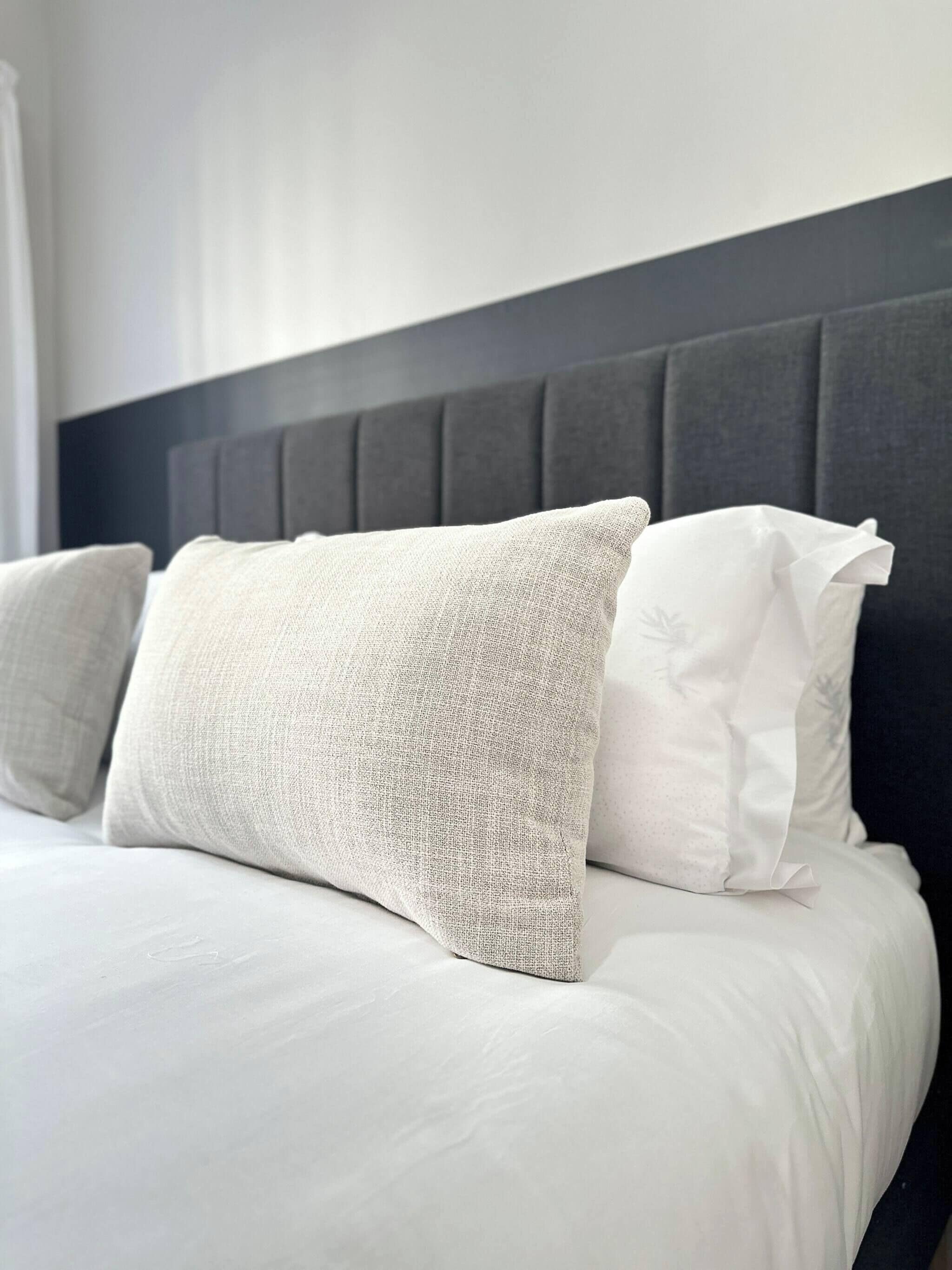 A bed with white bedding and two pillows, one with a textured pattern and the other plain.