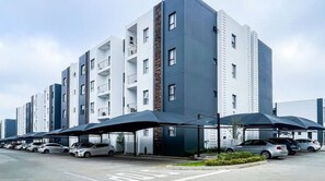 Ein mehrstöckiges Wohngebäude mit modernem Design, das Balkone und einen Parkplatz mit Autos zeigt.