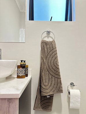 Un baño con un lavabo blanco, dos botellas de artículos de aseo, una toalla y un dispensador de papel higiénico.