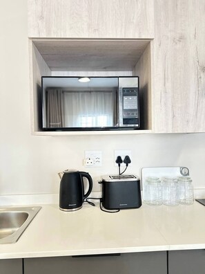 Eine Küchenzeile mit einer Mikrowelle, einem Toaster, einem Wasserkocher und Gläsern auf der Arbeitsfläche.