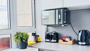 A compact kitchen with a built-in microwave, a coffee maker, and a toaster. A potted plant and a basket with tea bags are on the counter. - Top Floor Getaway With Cozy Canopy Bed (Edinburgh)