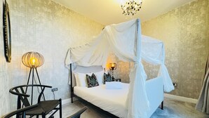 A bedroom with a four-poster bed, a bedside table with a lamp, a chair, and a decorative wall piece. - Top Floor Getaway With Cozy Canopy Bed (Edinburgh)