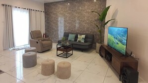 Un salon moderne comprenant un canapé, un fauteuil, des poufs, une table basse et un téléviseur posé sur un meuble en bois.
