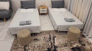Une chambre d’hôtel avec deux lits simples, une petite table de chevet avec une lampe, une commode et une grande fenêtre avec des rideaux.