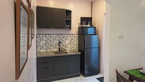 Une cuisine de taille réduite, dotée de meubles de rangement aux couleurs sombres, d’un four à micro-ondes encastré et d’un réfrigérateur.