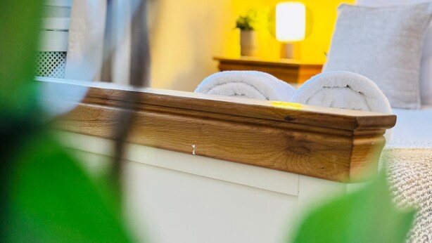 A neatly made bed with two towels, a bedside table with a lamp, and a small plant. - Top Floor Apartment with Castle Views (Edinburgh)