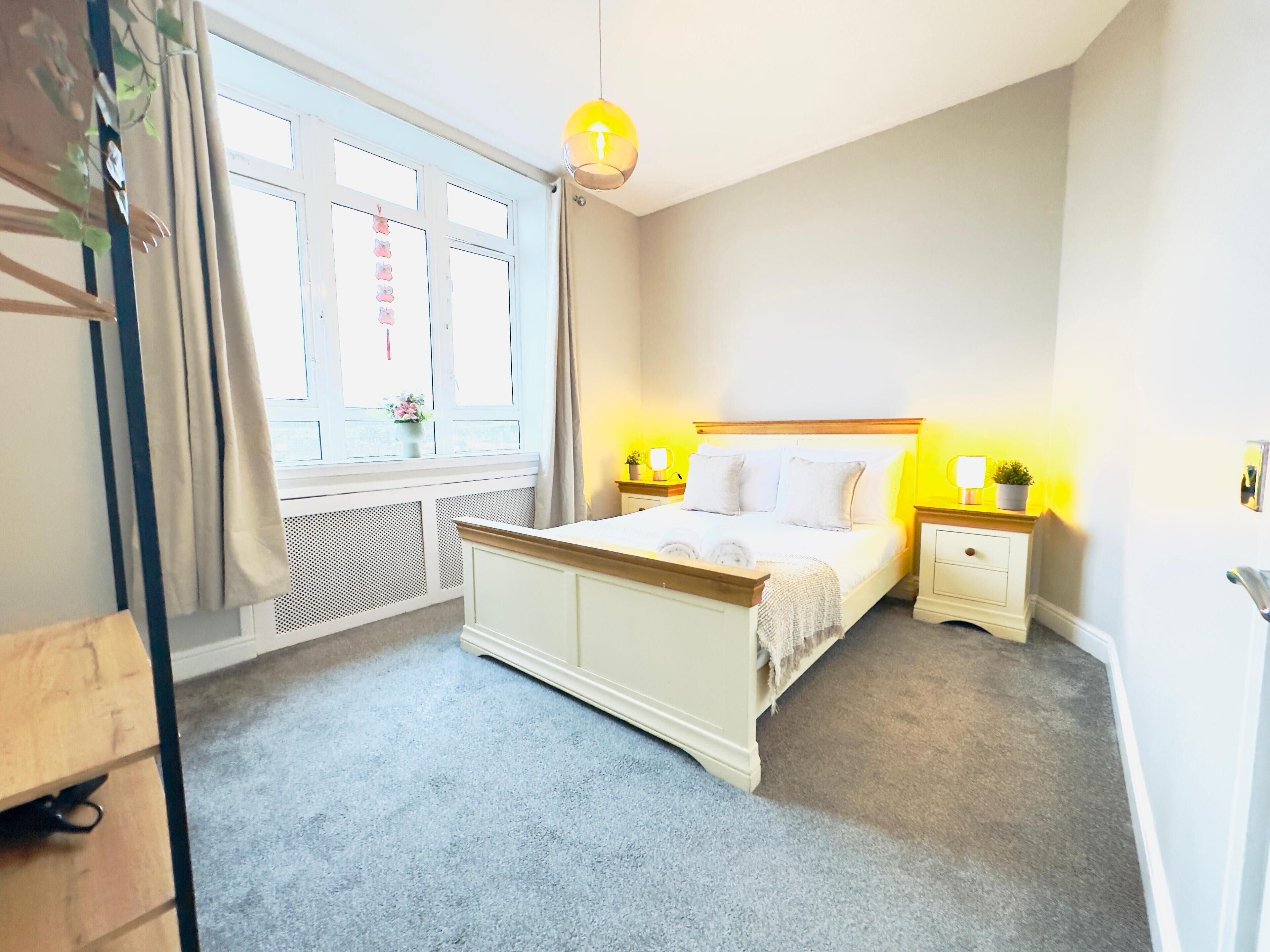 Une chambre à coucher avec un lit, des tables de chevet, une fenêtre avec des rideaux et un luminaire suspendu.