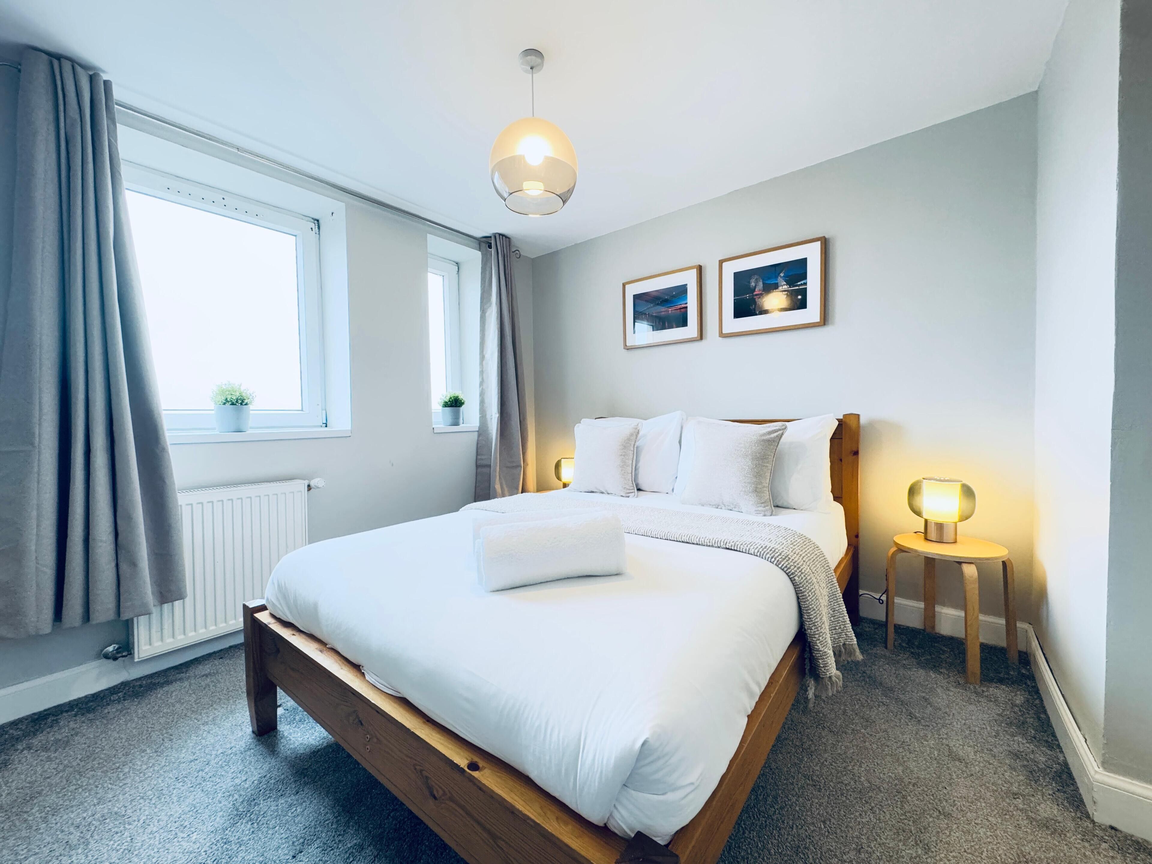 A bedroom with a wooden bed, a window with curtains, a radiator, and two bedside lamps.
