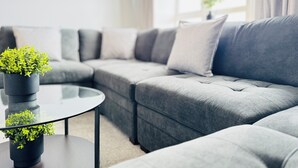 A modern living room with a grey sectional sofa, a glass coffee table, and a potted plant. - Skyline View Apartment (Edinburgh)