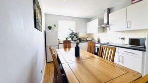 A modern kitchen with white cabinets, a wooden dining table, and a built-in microwave. - Skyline View Apartment (Edinburgh)