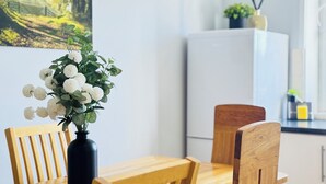 A dining area with a wooden table and chairs, a black vase with white flowers, and a white refrigerator in the background. - Skyline View Apartment (Edinburgh)