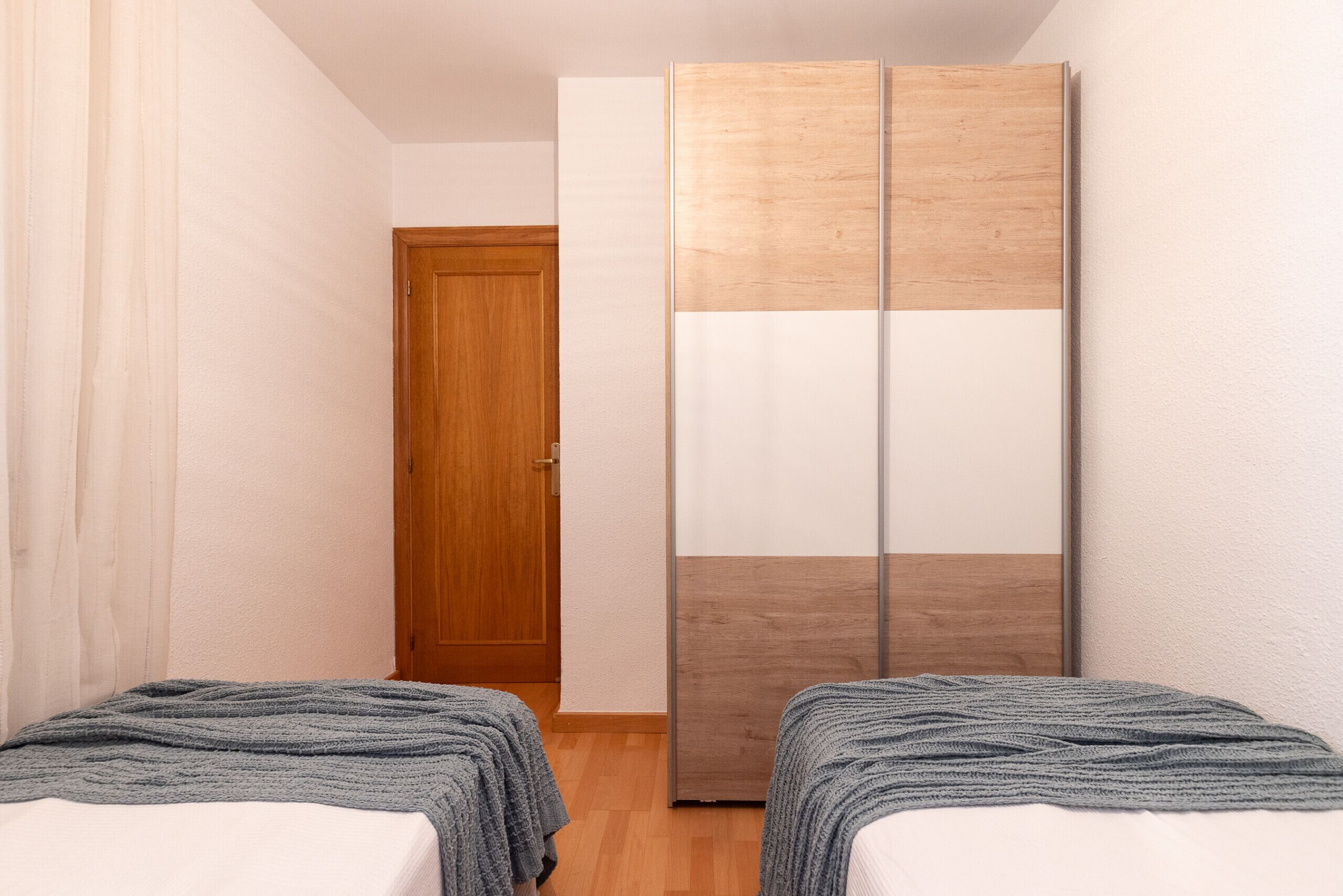 A bedroom with two single beds, a wooden wardrobe, and a door in the background.