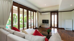 Amplia sala de estar con un sofá grande, un televisor y vistas al exterior a través de grandes ventanales.
