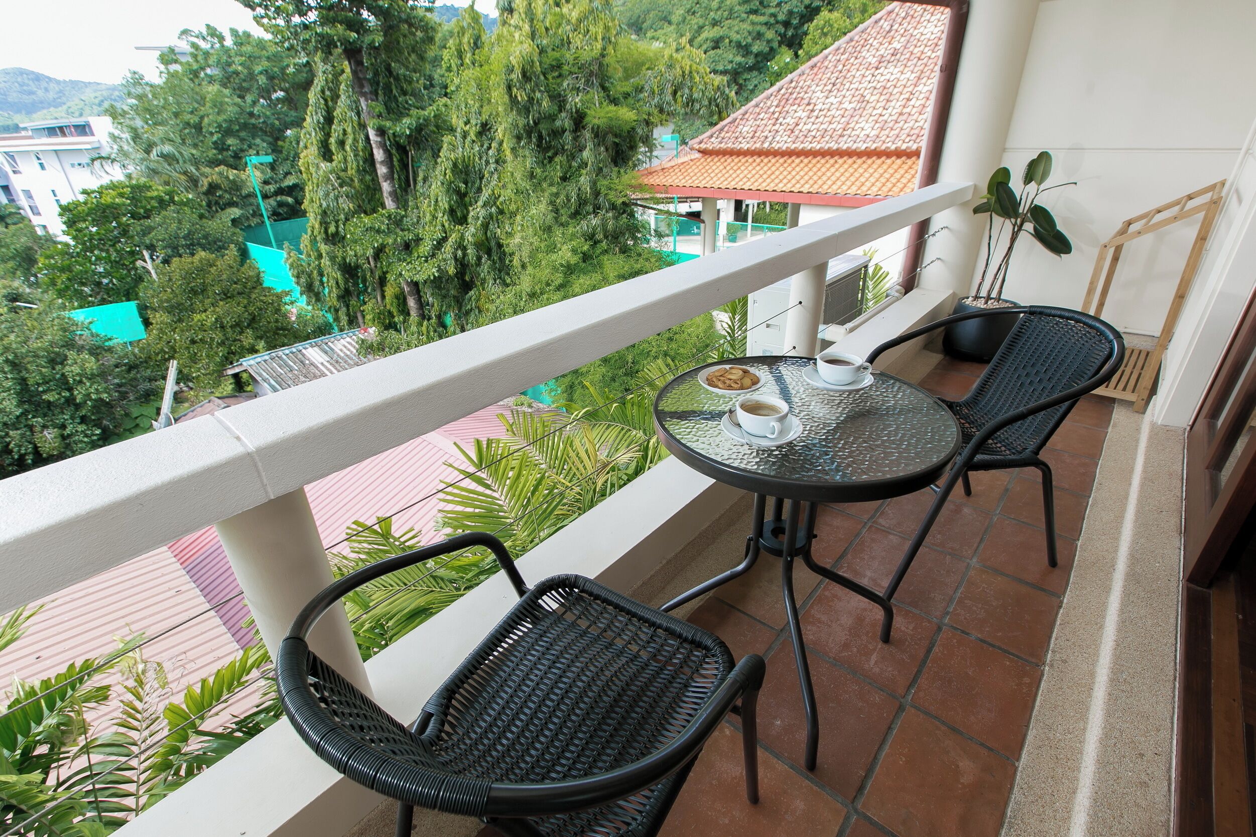 Un balcon avec deux fauteuils en osier, une petite table ronde avec une tasse et une soucoupe, et une plante en pot.