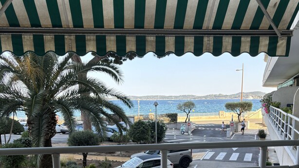 Eine Terrasse mit Tisch und Stühlen, die auf eine Straße mit geparkten Autos und Meerblick blickt.