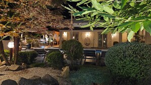 An outdoor seating area with tables and chairs, surrounded by greenery and a small water feature.