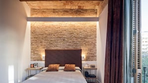A bedroom with a brick wall, a wooden ceiling, a large bed, two bedside tables, and a view of greenery through a window. - Pau Claris Design Apt. Next to Paseo de Gracia (Barcelona)