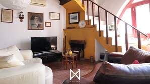 A living room with a TV, sofa, and coffee table. There is a fireplace and a staircase leading to an upper level. - MyStay - A Casa do Visconde (Mertola)