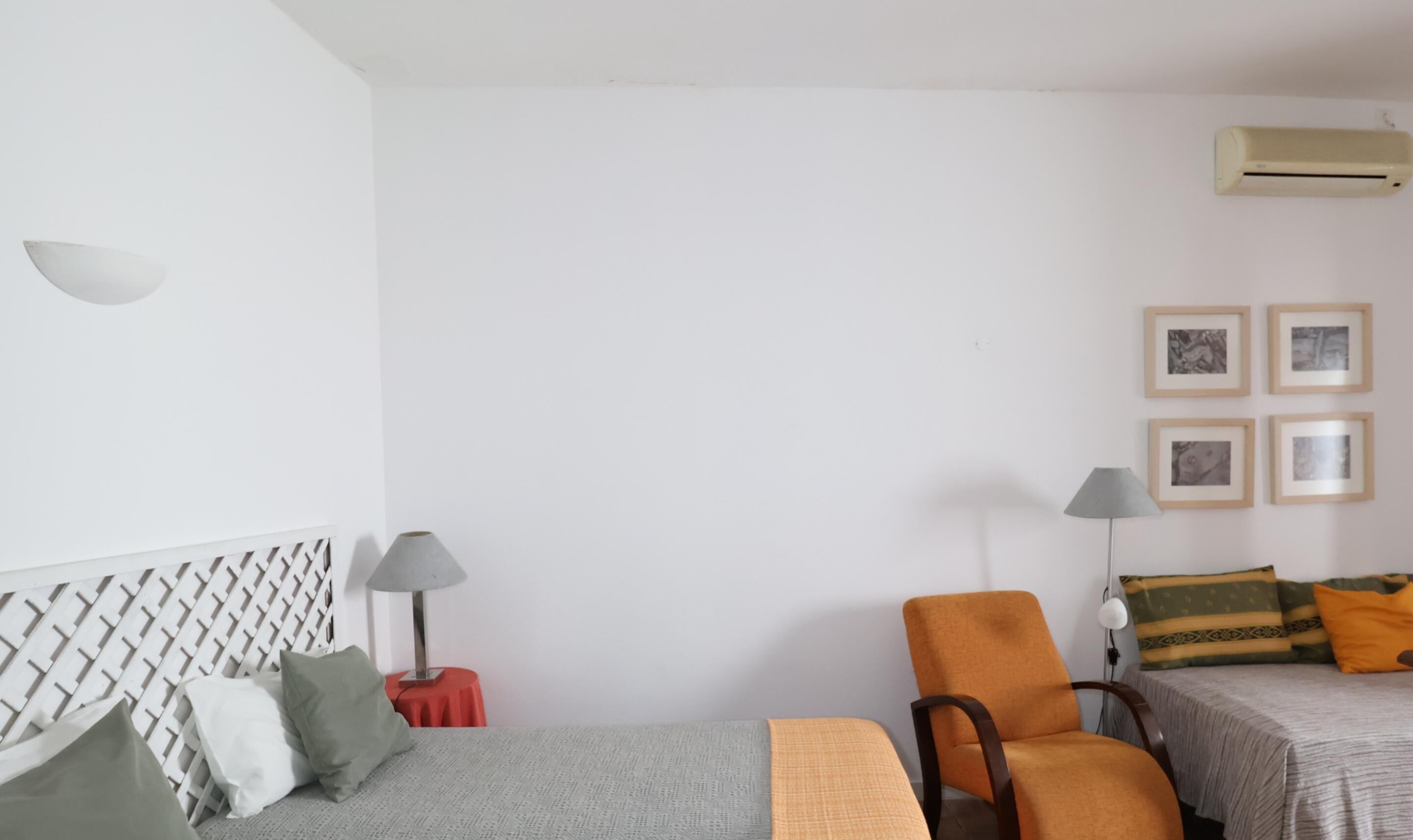 A simple, clean room with a bed, a chair, a small table, and a wall-mounted air conditioner.