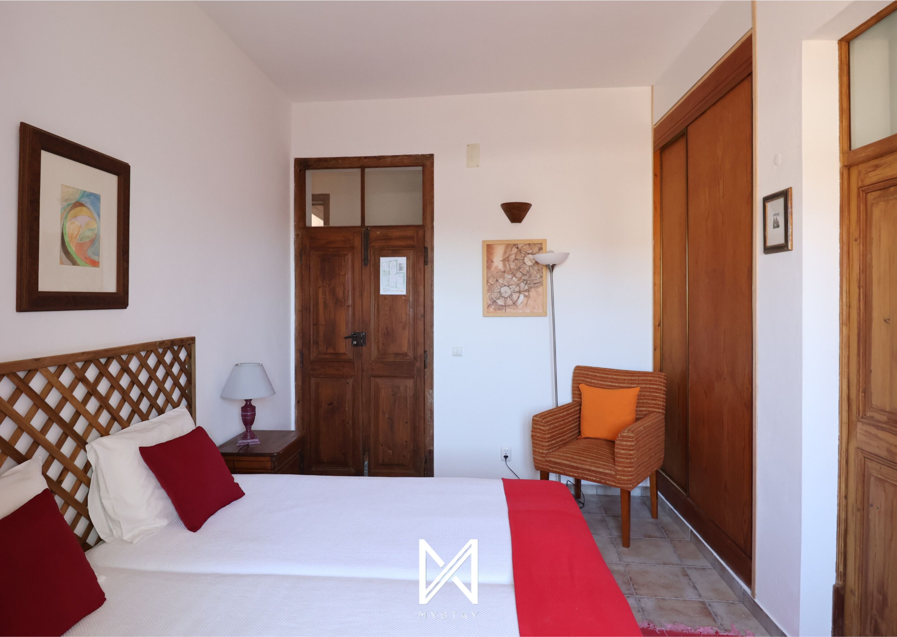 Un dormitorio con cama, armario de madera, una silla y una puerta.