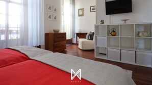 A modern bedroom with a large bed, a wooden dresser, a white shelving unit, and a flat-screen TV mounted on the wall. - MyStay - A Casa do Visconde (Mertola)