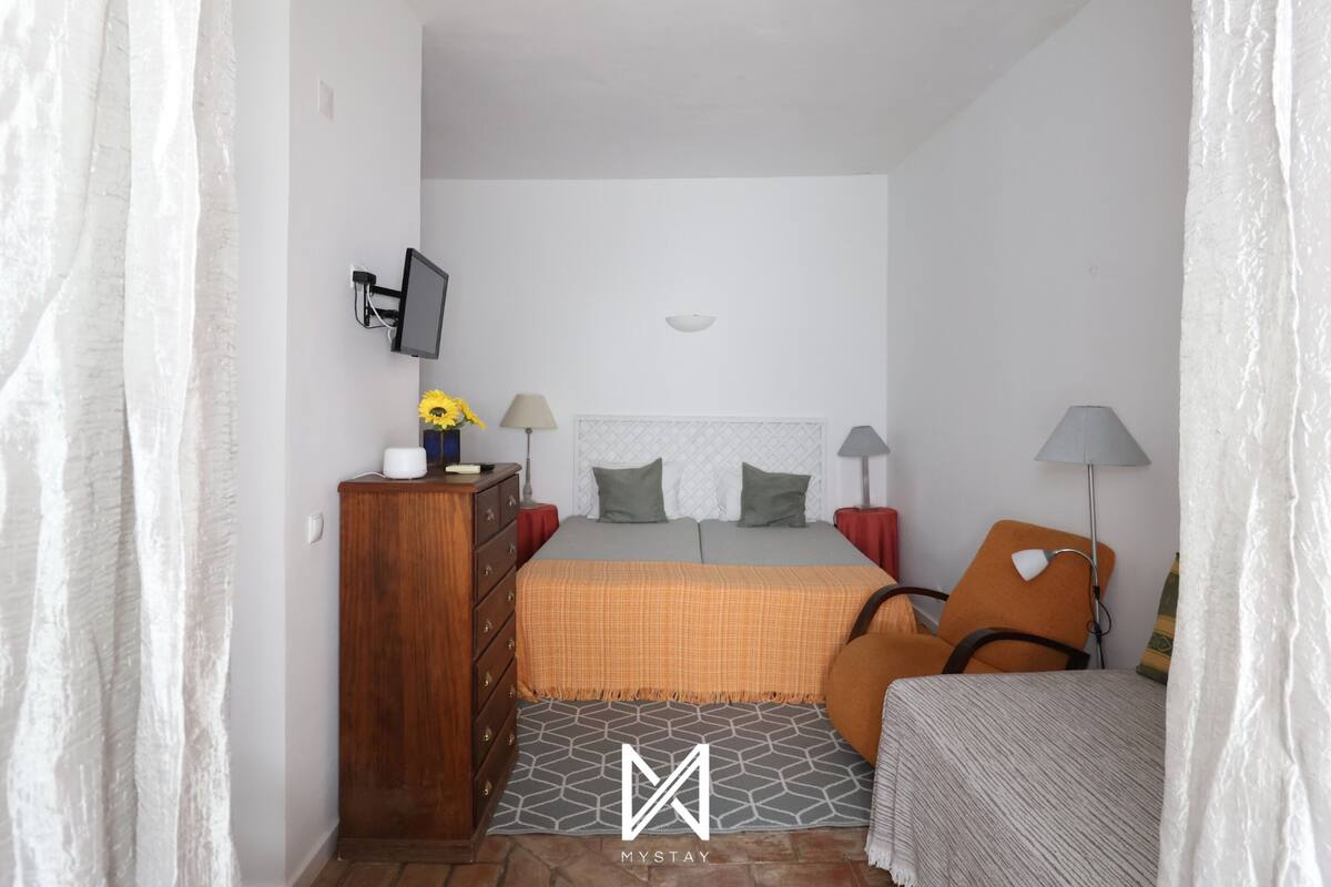 A bedroom with a bed, dresser, TV, lamps, and a small table with flowers.