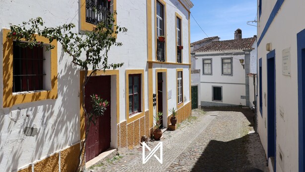 A narrow cobblestone street lined with traditional buildings, featuring balconies with potted plants and a clear blue sky. - MyStay - A Casa do Visconde (Mertola)