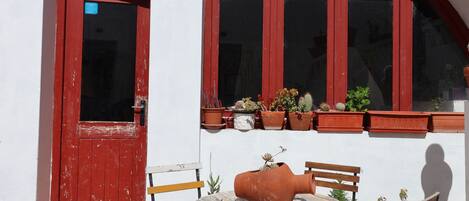 Une porte rouge avec une fenêtre au-dessus, une petite table avec des chaises et des plantes en pot sur le rebord de la fenêtre.