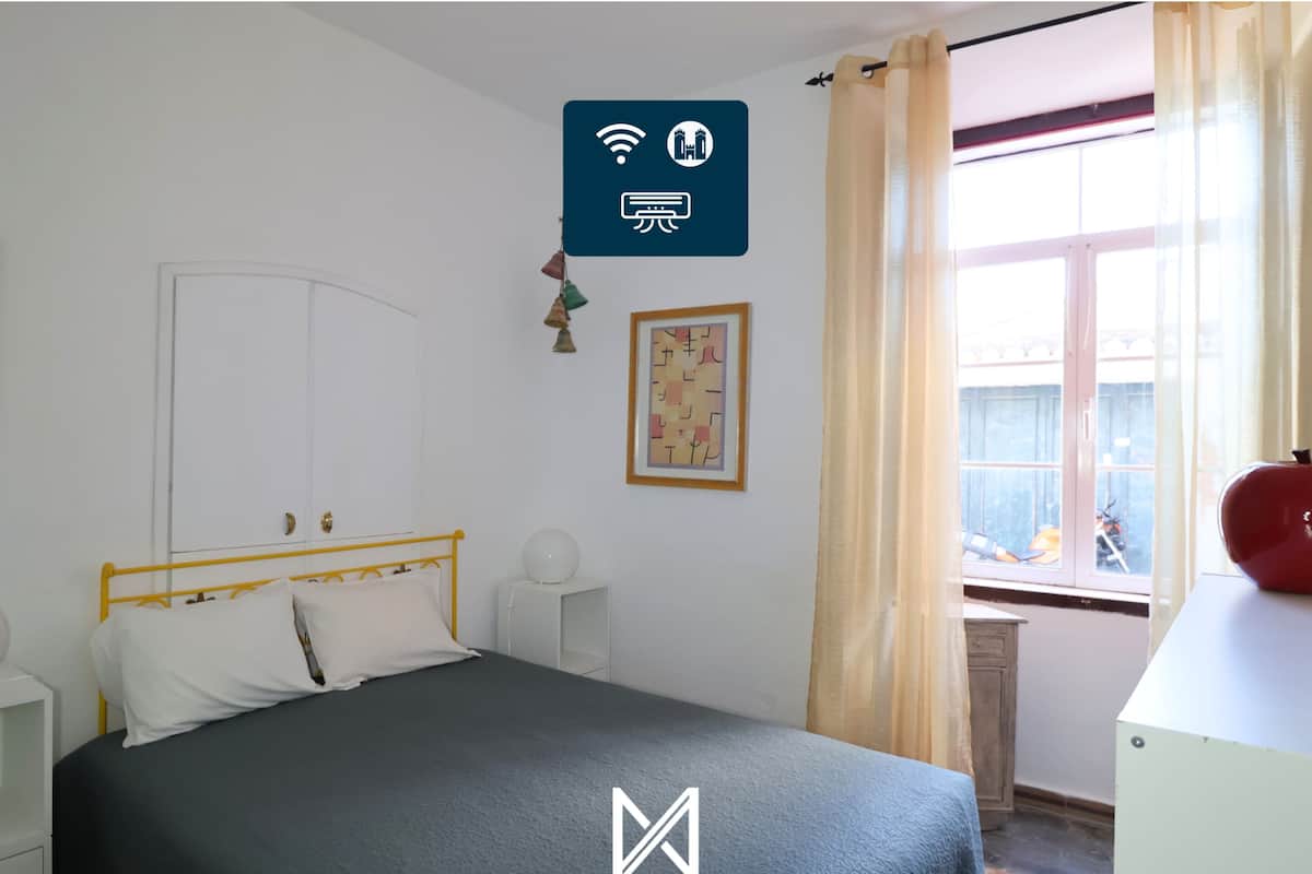A bedroom with a bed, bedside tables, a window with curtains, a radiator, and a wall-mounted sign indicating Wi-Fi availability.
