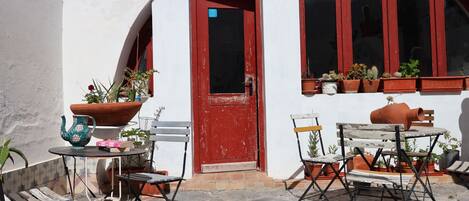 An outdoor patio with a red door, potted plants, and outdoor furniture.