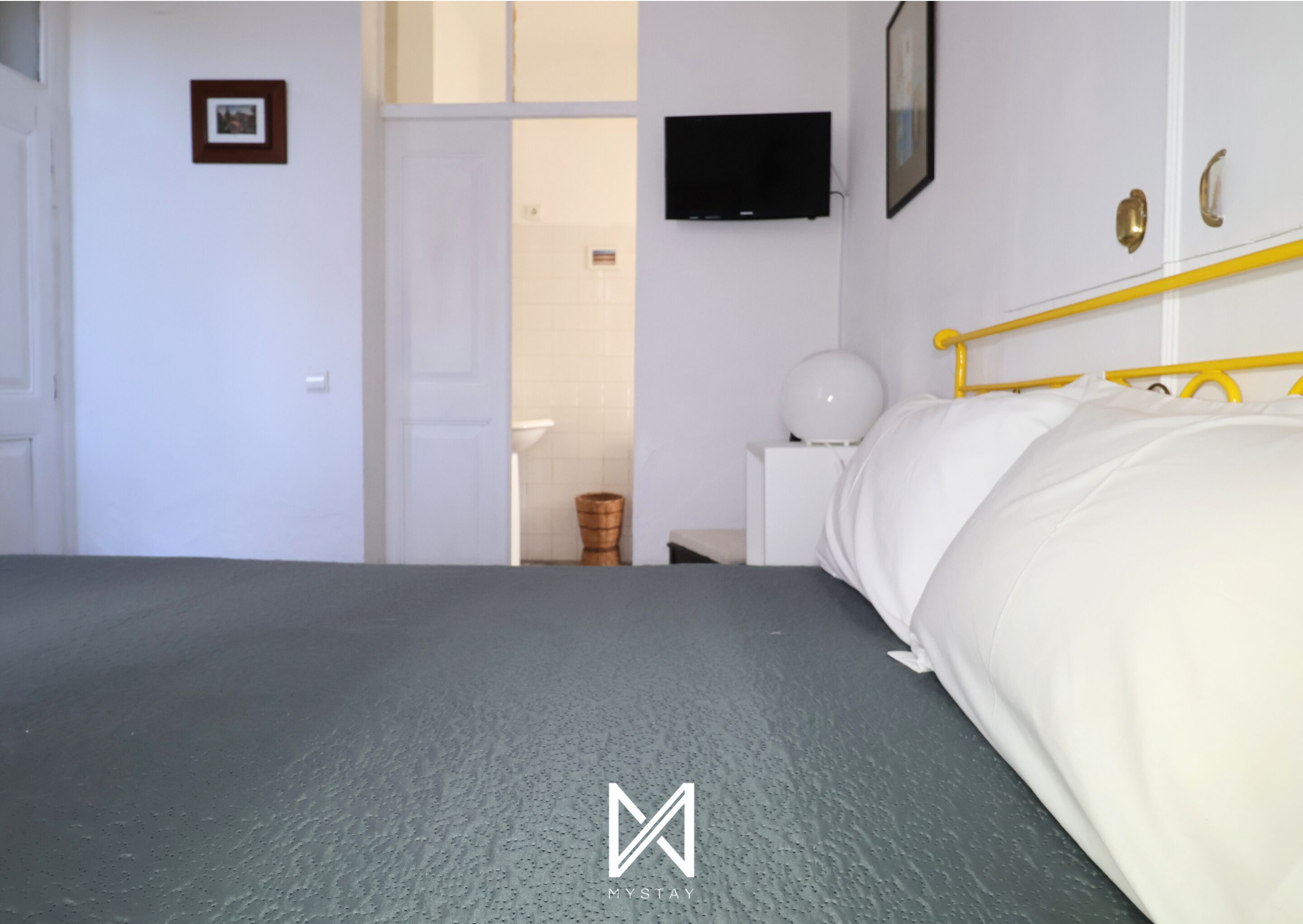 Een hotelkamer met een bed, een televisie aan de muur, een nachtkastje met een lamp en een deur naar een badkamer.