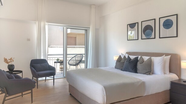 Ein modernes Hotelzimmer mit einem großen Bett, einer Sitzecke mit einem Sessel und einem kleinen Tisch sowie einem Balkon mit einem Stuhl.