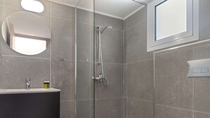 Ein modernes Badezimmer mit Duschkabine aus Glas, einem runden Spiegel und einem Fenster über dem Waschbecken.
