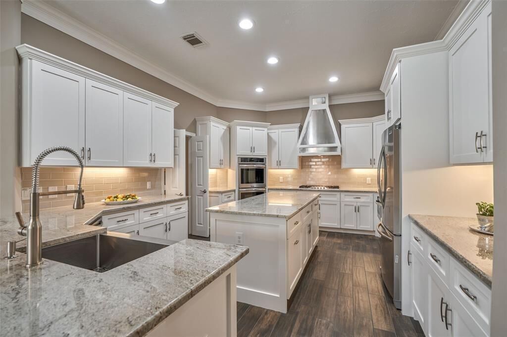 A modern kitchen with white cabinetry, a stainless steel range hood, and a central island.