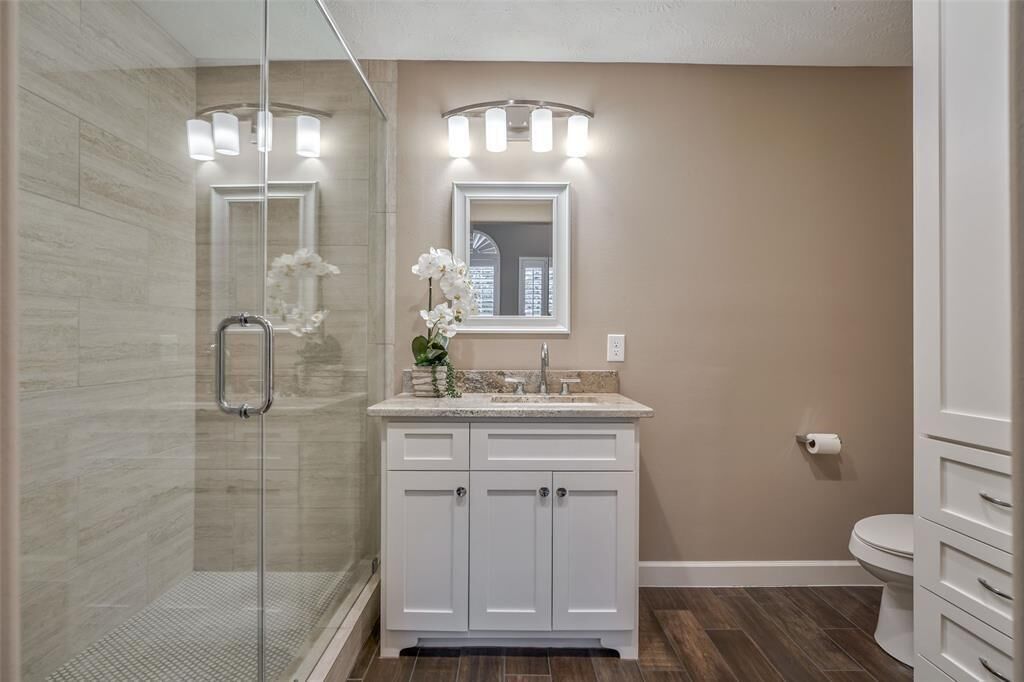 Une salle de bain avec une douche à parois de verre, un meuble-lavabo avec un miroir et des toilettes.