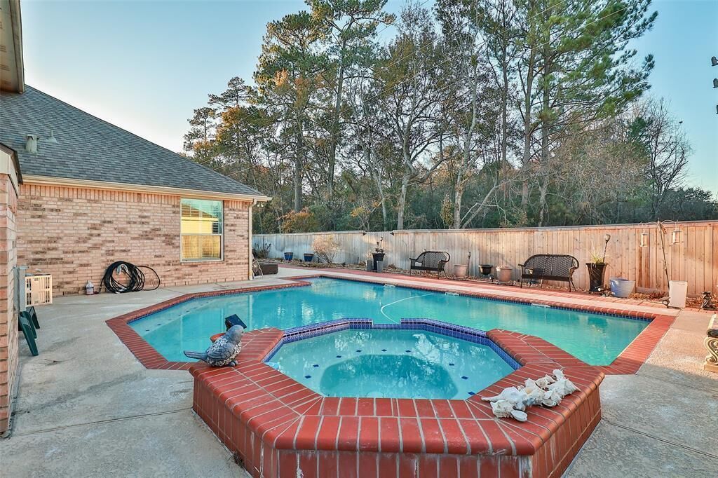 A backyard with a swimming pool, a hot tub, and a brick patio.