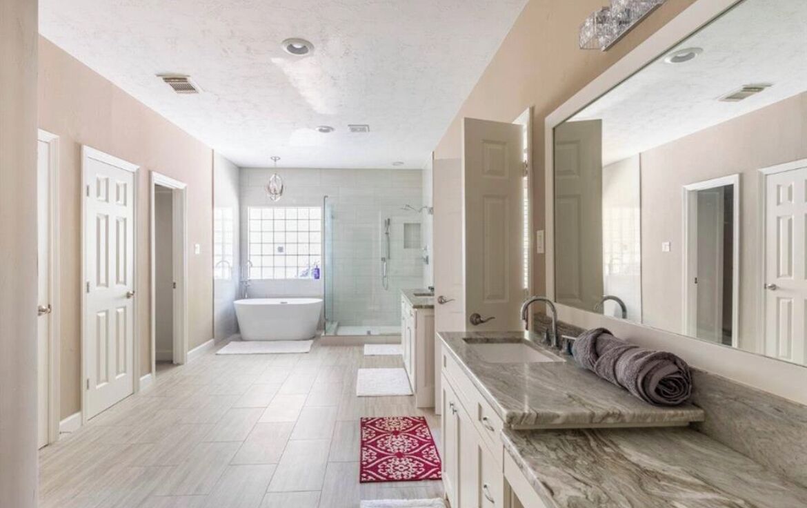 A spacious bathroom with a large bathtub, a vanity with a mirror, and a red patterned rug on the floor.