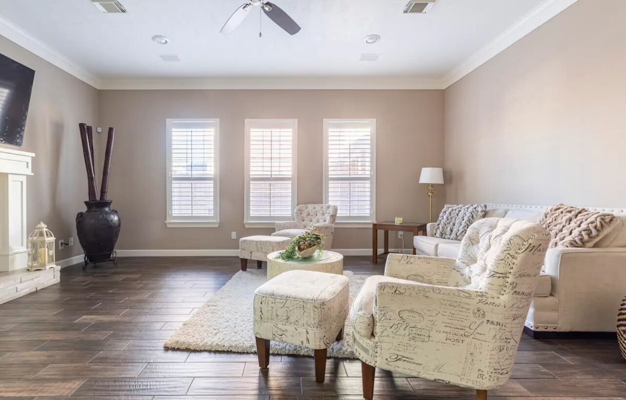 A spacious living room with a fireplace, three windows, a ceiling fan, and a large sofa.